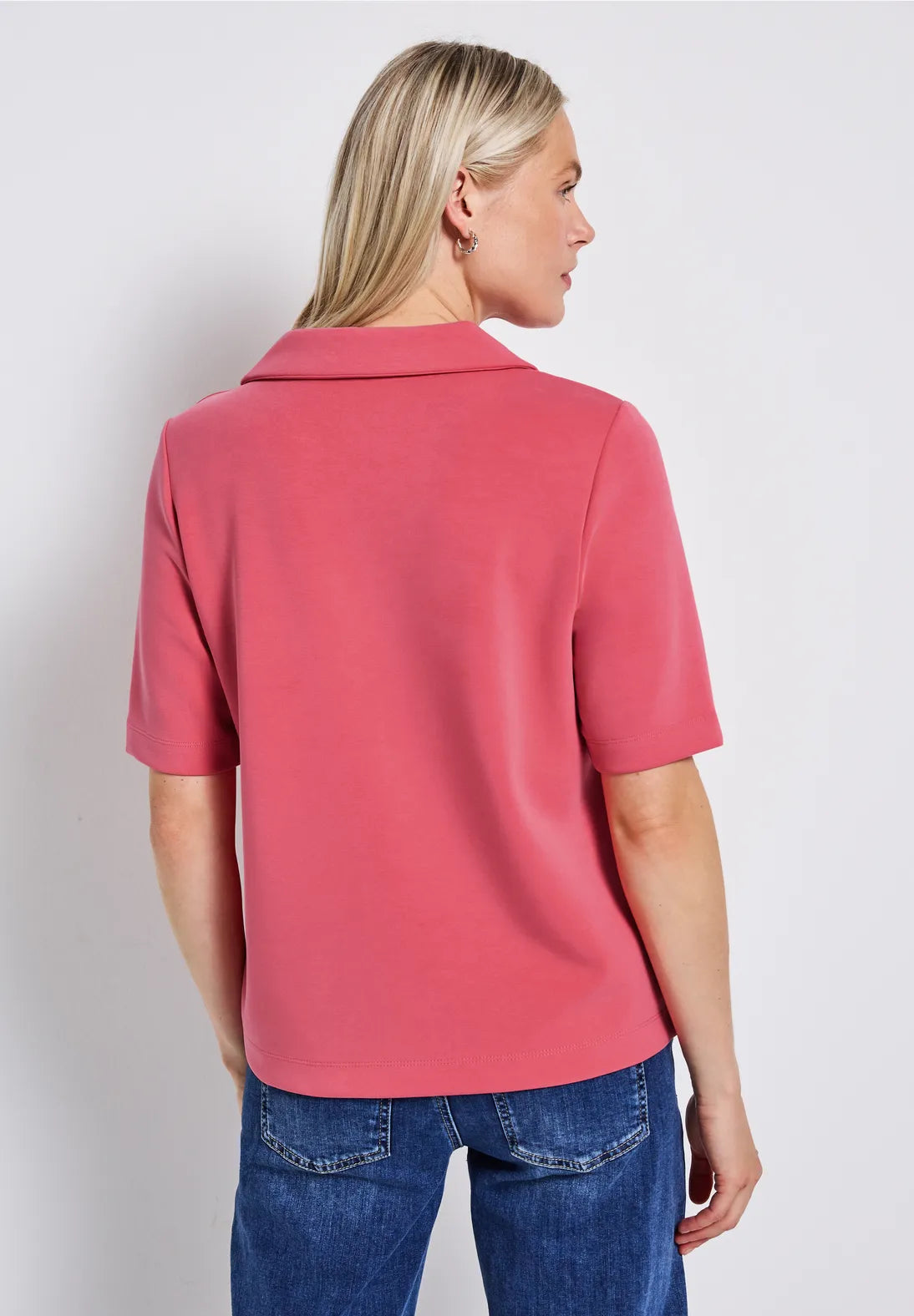 Woman wearing a pink polo shirt and blue jeans against a white background