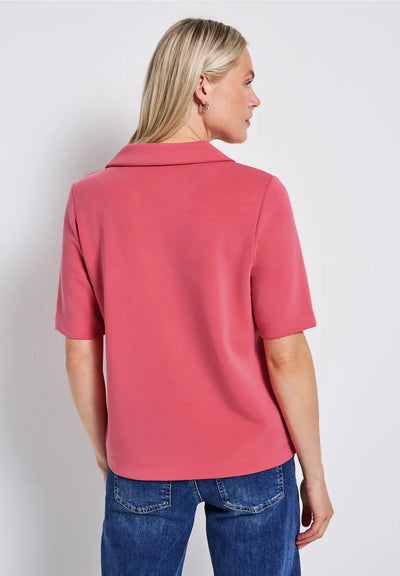 Woman wearing a pink polo shirt and blue jeans against a white background
