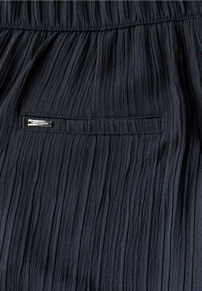 Close-up of dark blue pleated pants with a brand label.