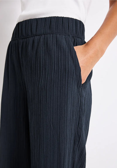 Navy pleated pants worn with a white top on a light background