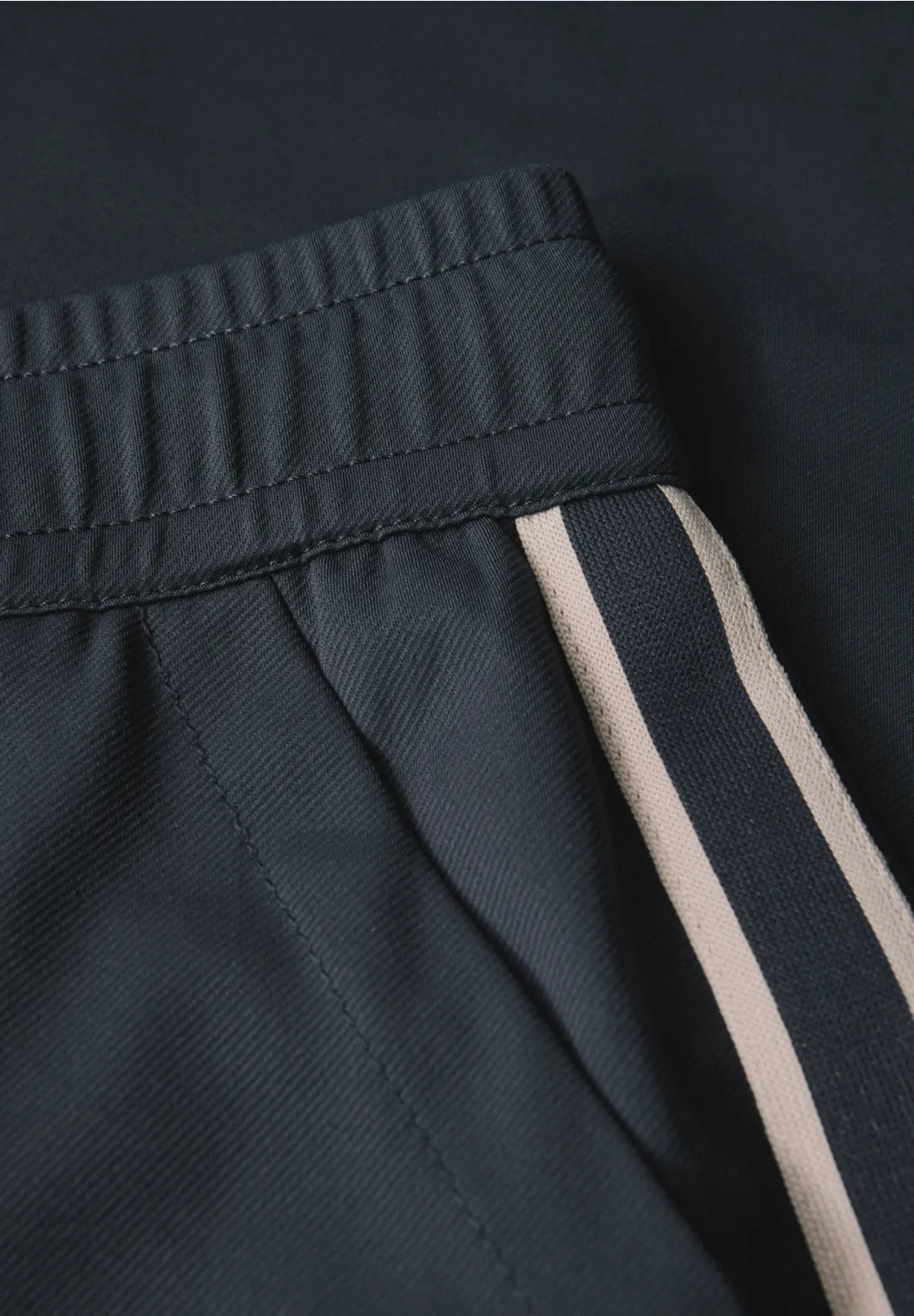 Close-up of dark pants with a beige stripe on a black background