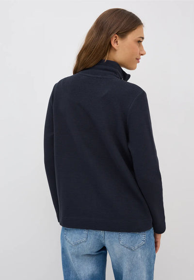 Woman wearing a navy blue jacket and light blue jeans on a white background