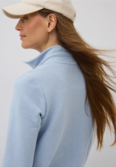 Woman wearing a light blue sweater and beige cap on a plain background
