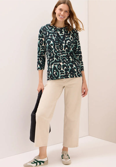 Woman wearing a patterned top and beige pants against a white background