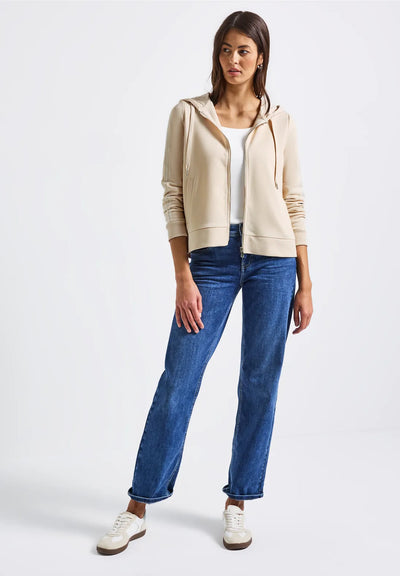 Woman wearing a beige cardigan, white shirt, and blue jeans on a white background