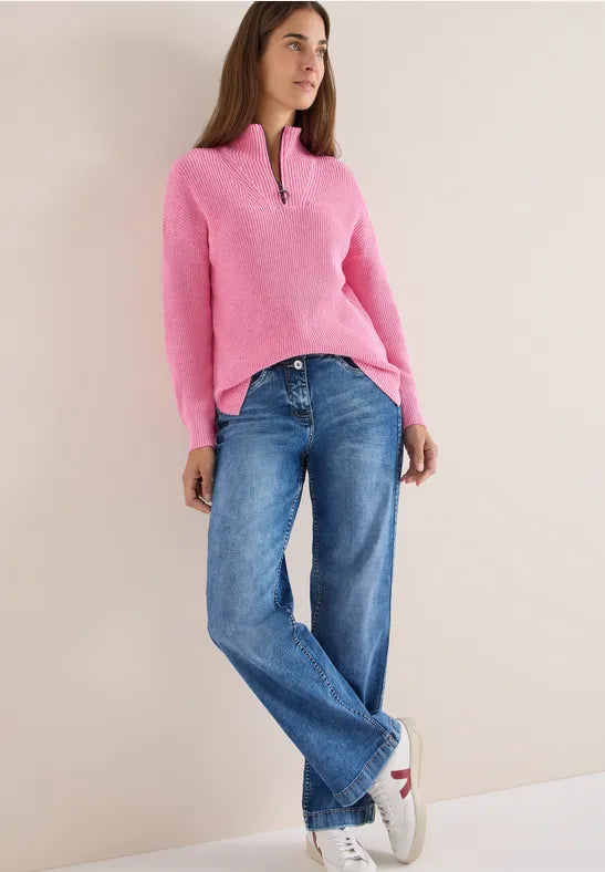 Woman wearing a pink sweater and blue jeans against a beige background