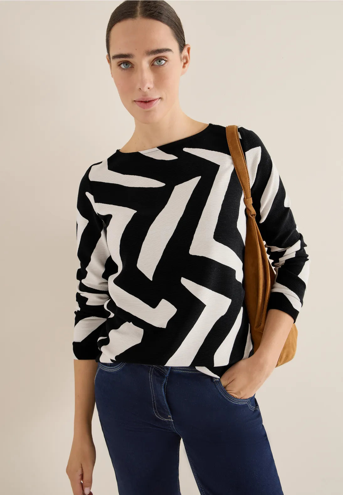 Woman wearing a black and white patterned sweater with a brown bag on a beige background