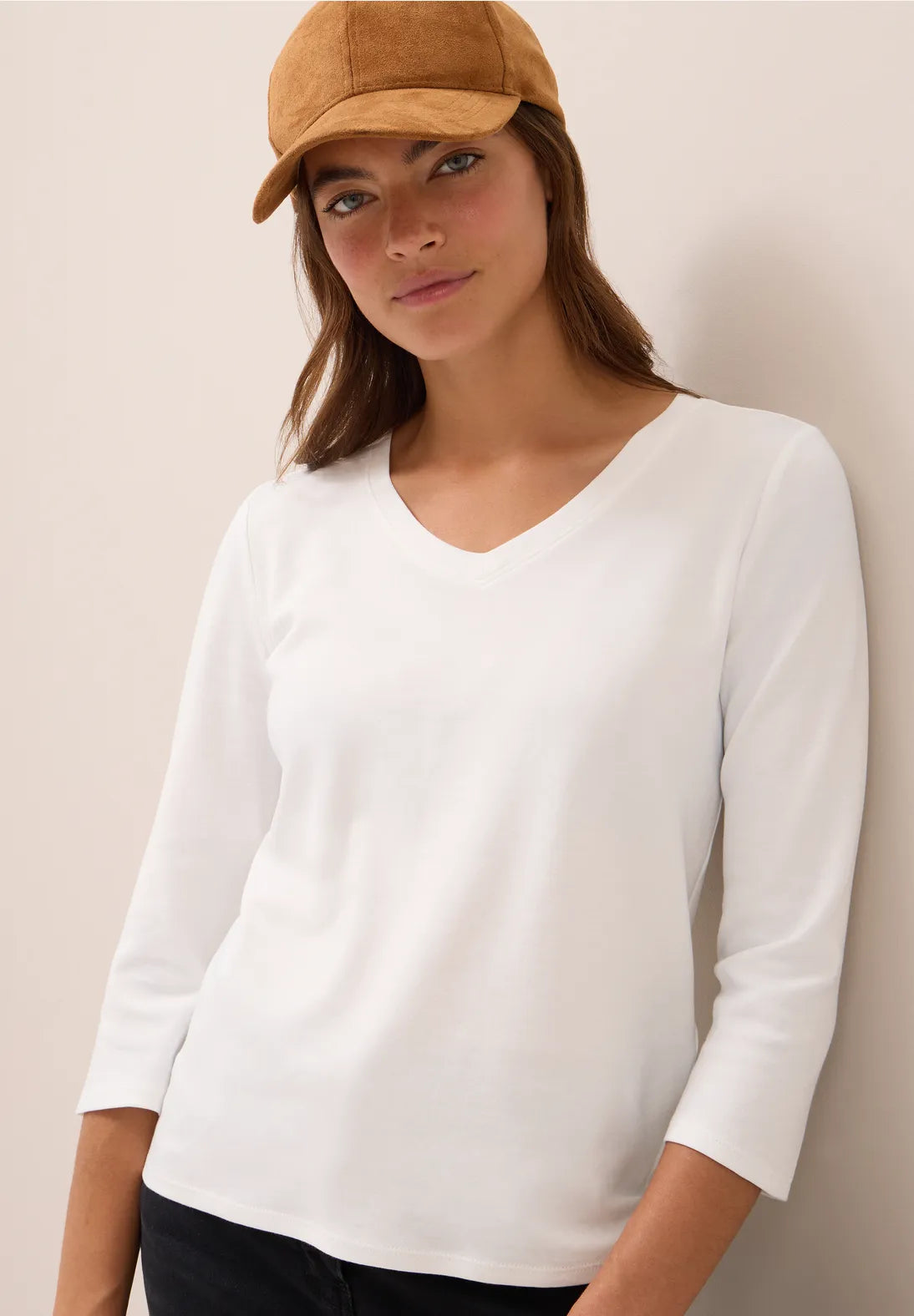 Woman wearing a white long-sleeve shirt and a brown cap against a plain background