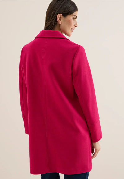 Woman wearing a bright pink coat on a beige background