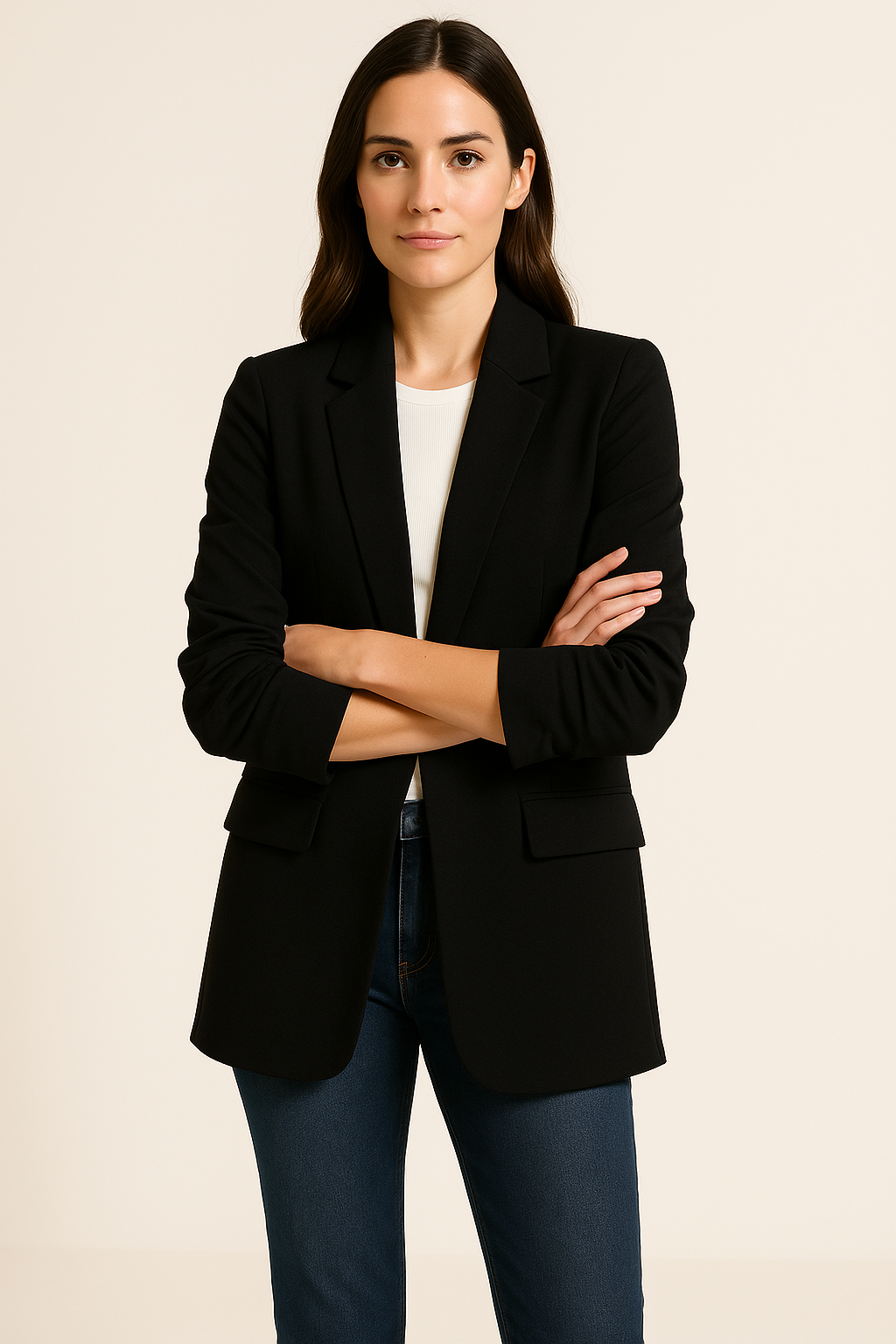 Woman wearing a black blazer over a white shirt and blue jeans on a beige background