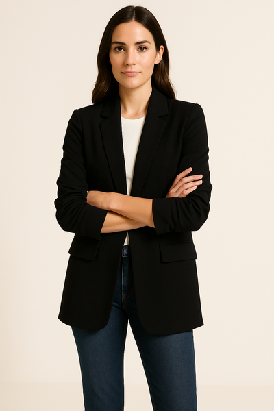 Woman wearing a black blazer over a white shirt and blue jeans on a beige background