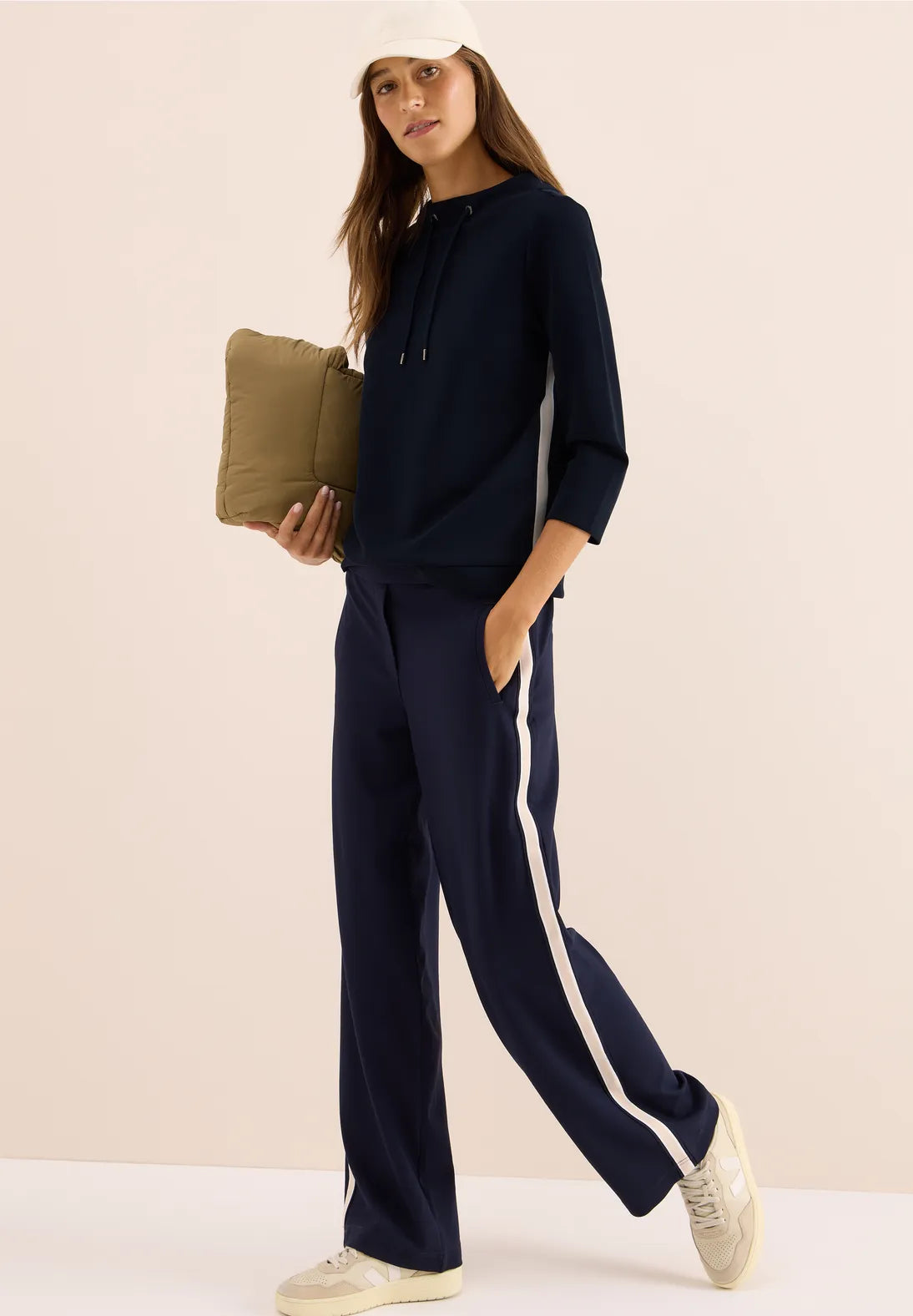 Woman wearing a navy tracksuit with white stripes on a beige background