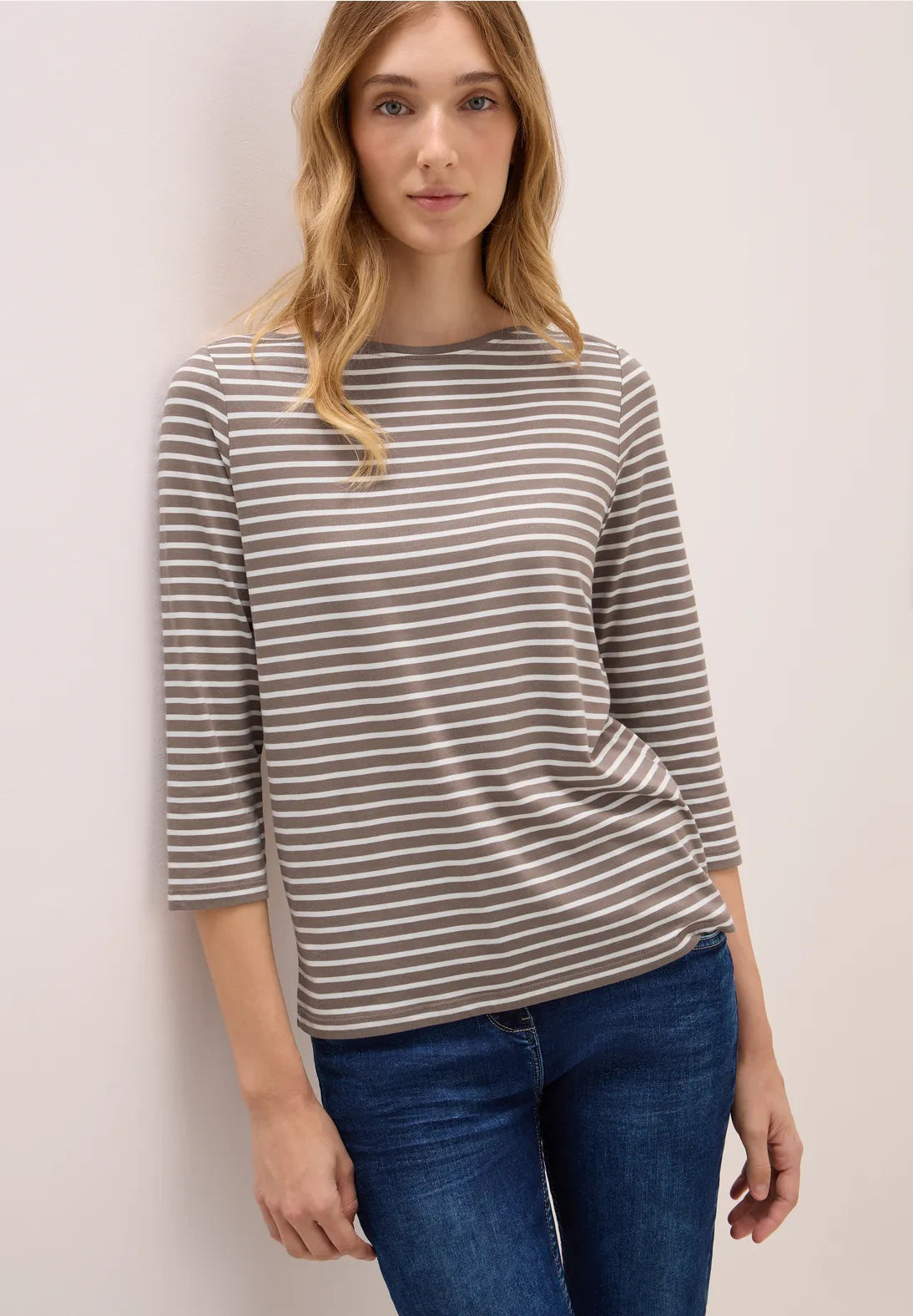 Woman wearing a striped sweater and jeans against a plain background