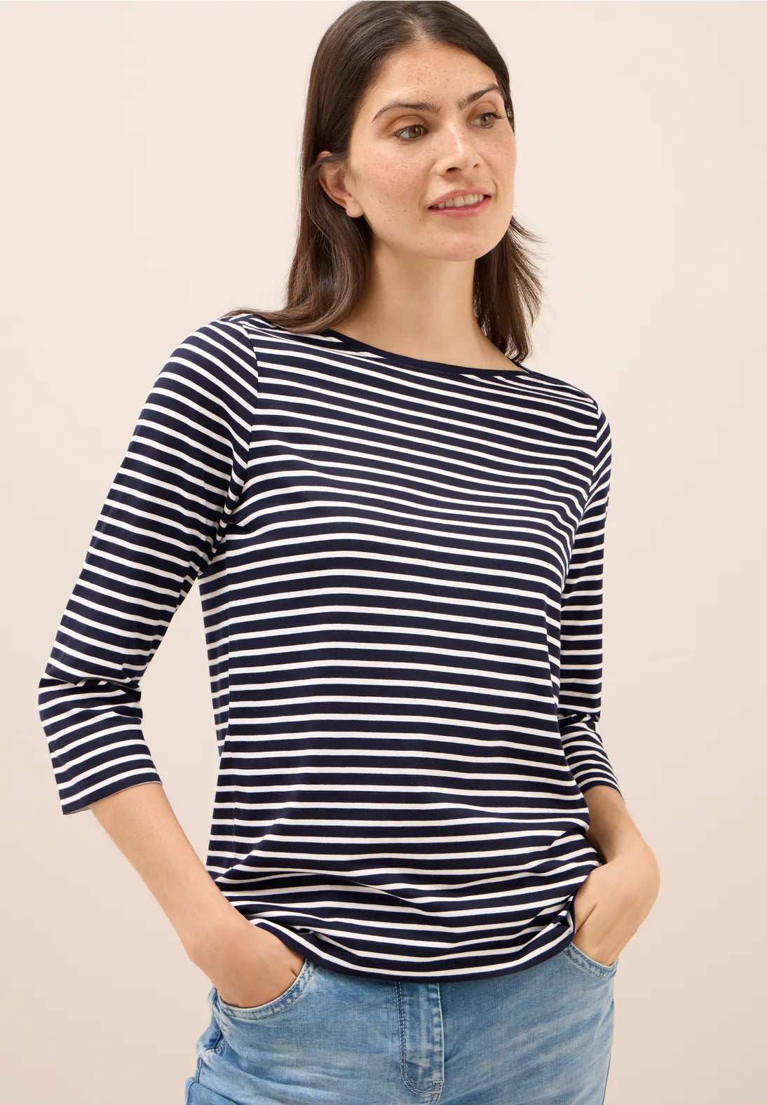 Woman wearing a navy and white striped shirt with blue jeans on a beige background