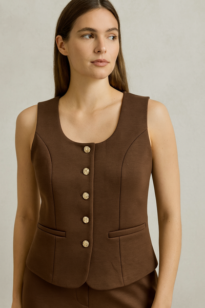 Woman wearing a brown sleeveless blazer with buttons on a neutral background