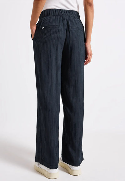 Person wearing dark blue pleated pants on a white background