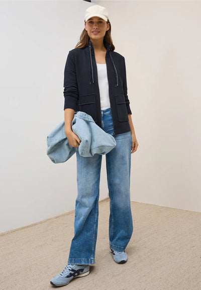 Person wearing a black jacket, white shirt, blue jeans, and a white cap, holding a denim jacket.