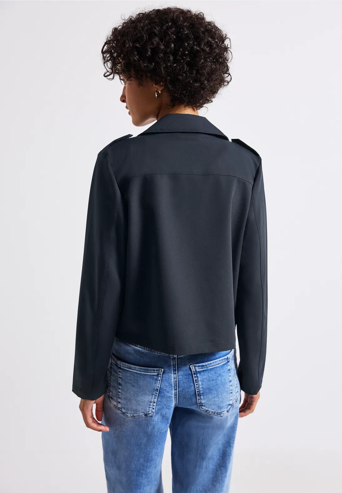 Person wearing a black jacket and blue jeans on a white background