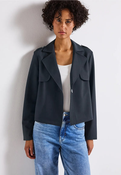 Woman wearing a dark blue jacket and blue jeans against a white background