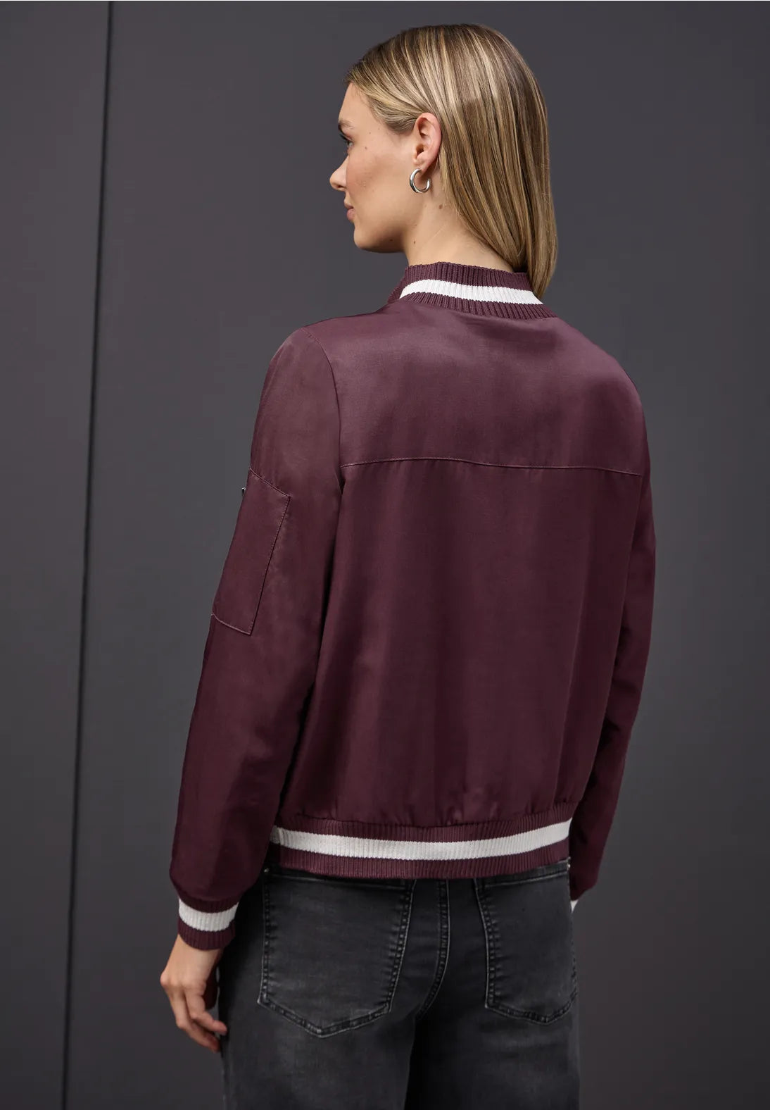 Person wearing a burgundy jacket with white trim on a gray background