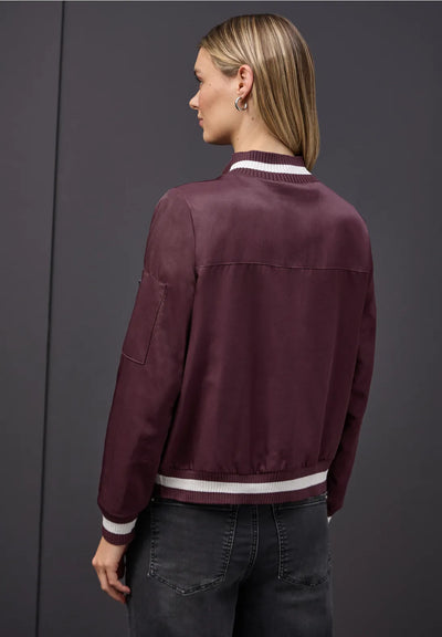 Person wearing a burgundy jacket with white trim on a gray background