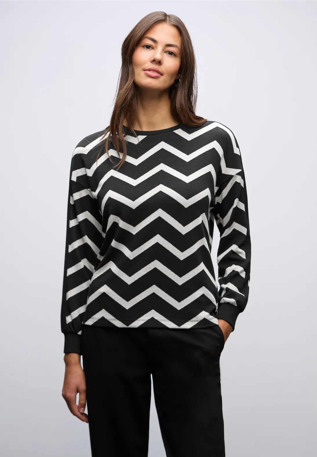 Woman wearing a black and white zigzag patterned sweater on a plain background