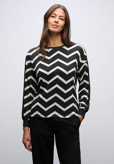 Woman wearing a black and white zigzag patterned sweater on a plain background