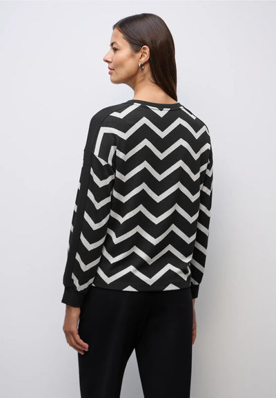 Woman wearing a black and white zigzag patterned sweater against a plain background