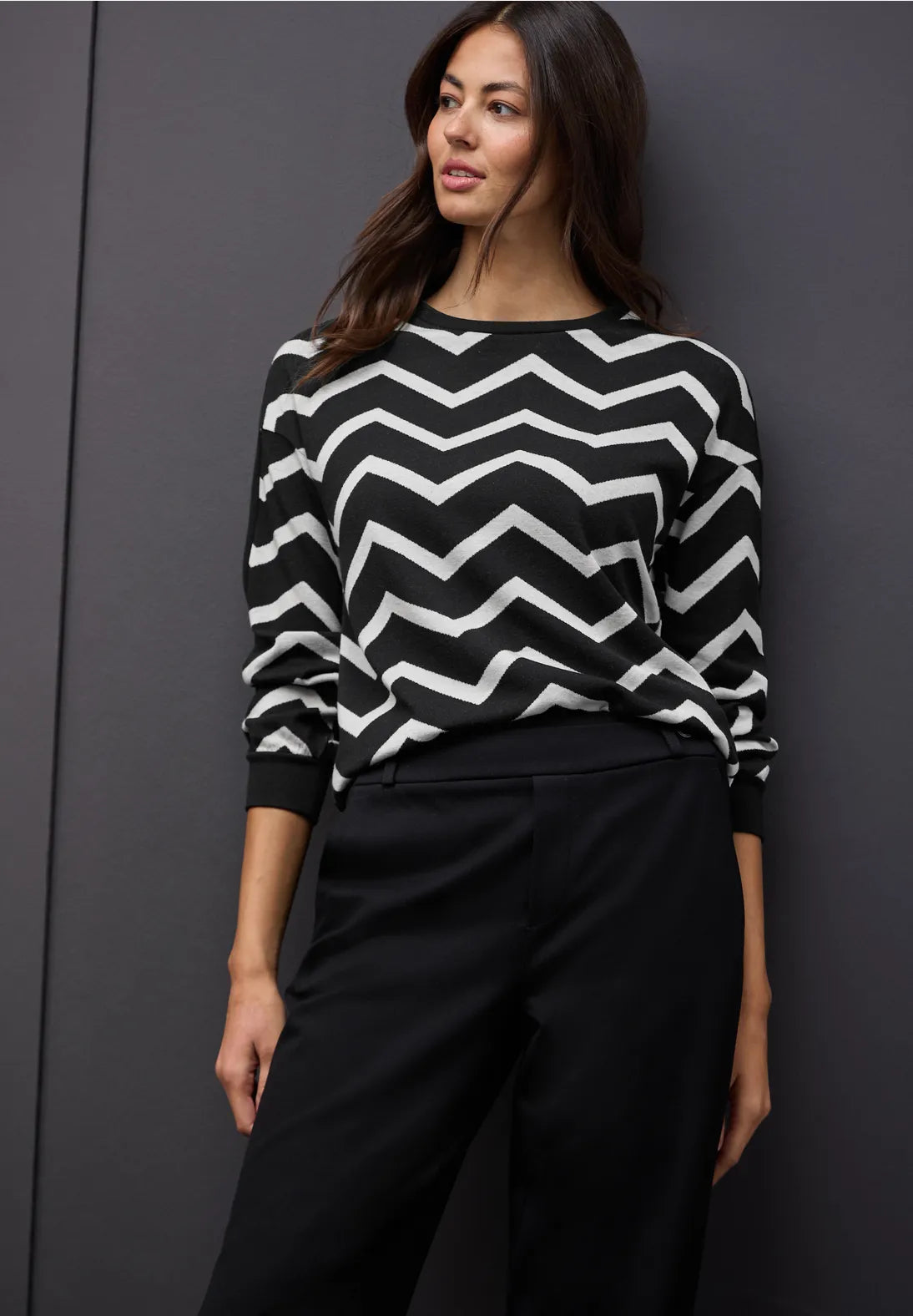 Woman wearing a black and white zigzag sweater against a dark background