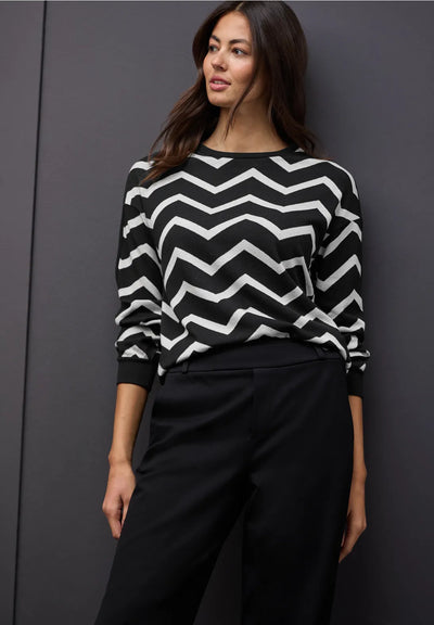 Woman wearing a black and white zigzag sweater against a dark background