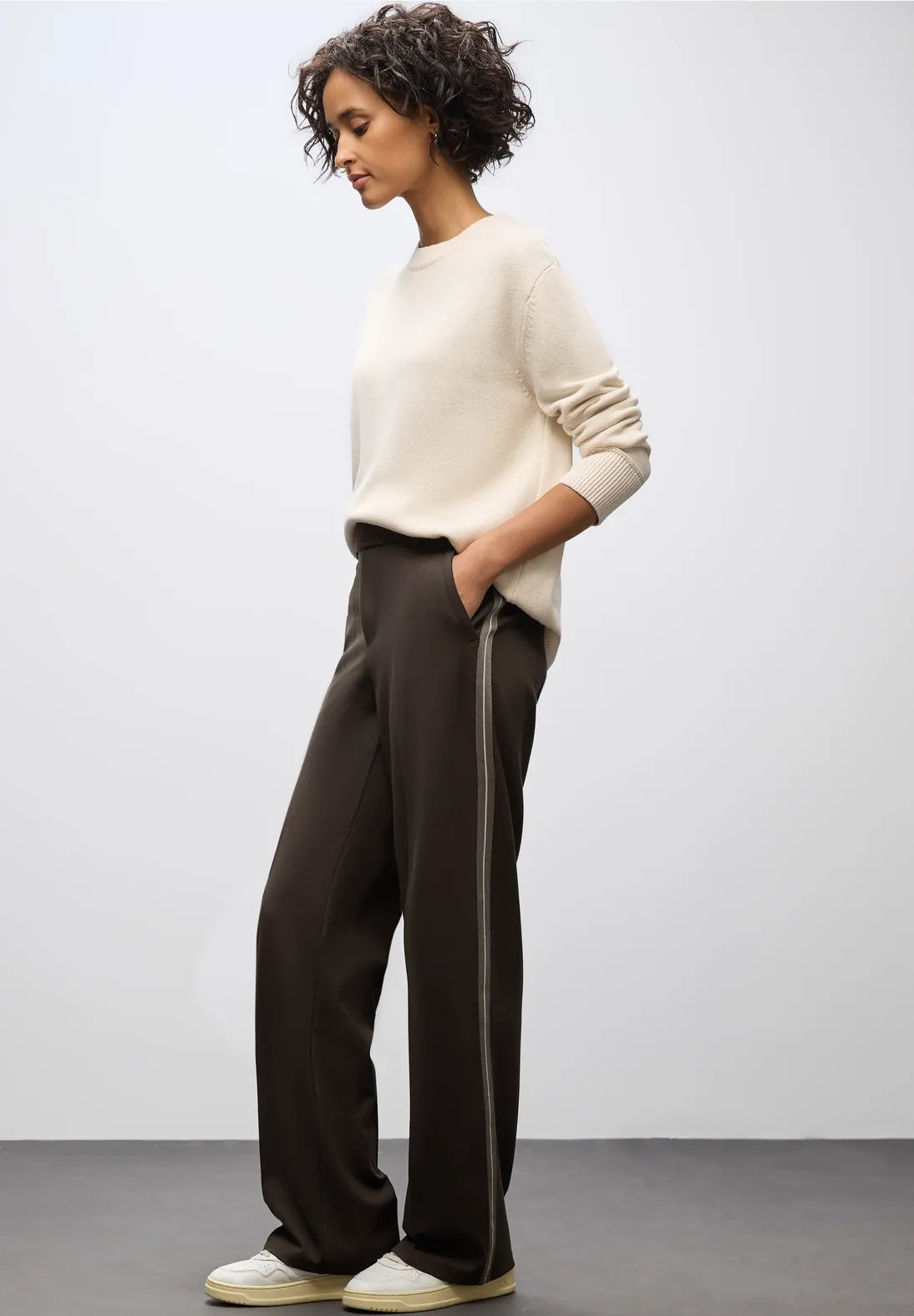 Woman wearing a white sweater and dark pants against a plain background