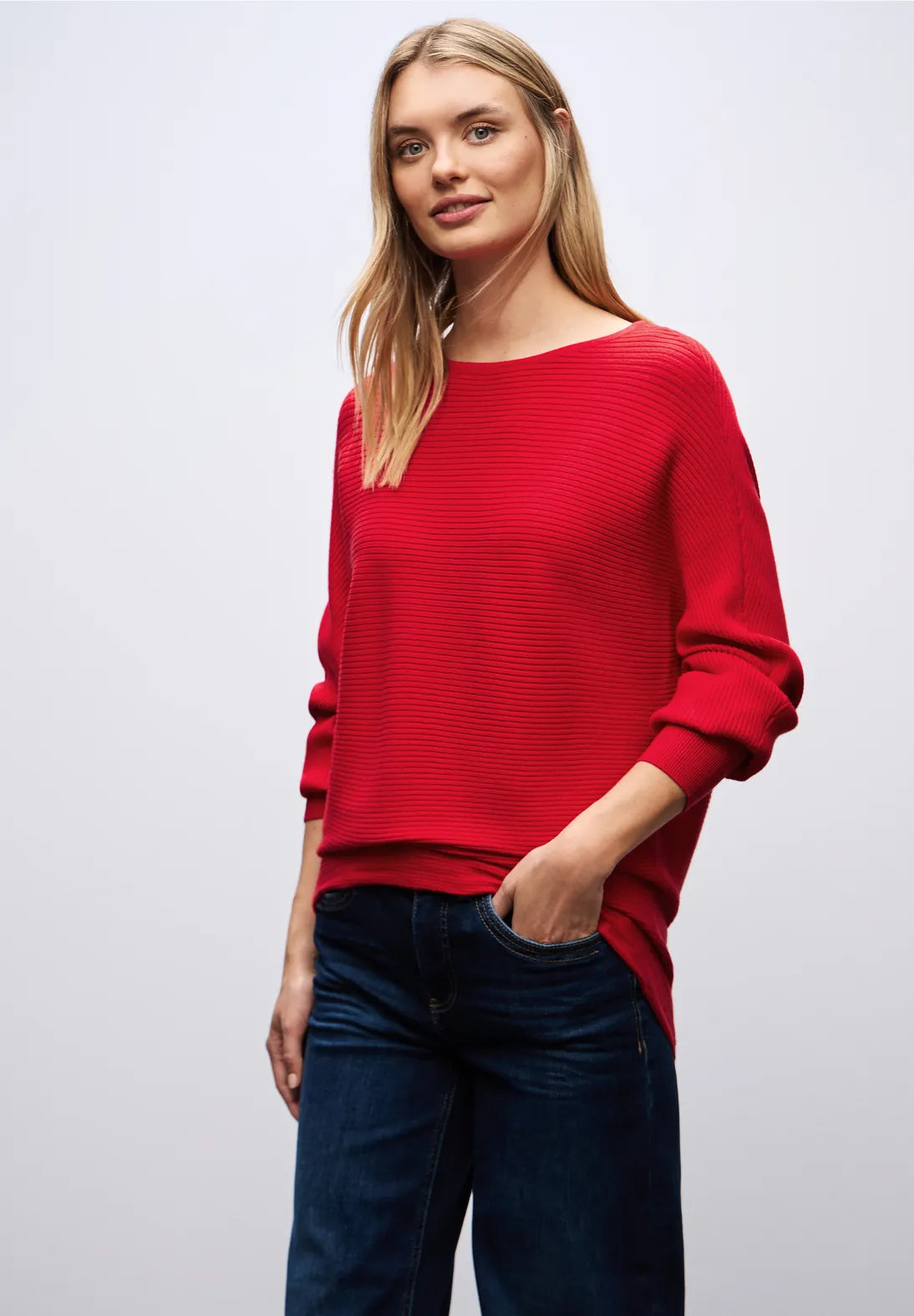 Woman wearing a red sweater and dark jeans on a white background