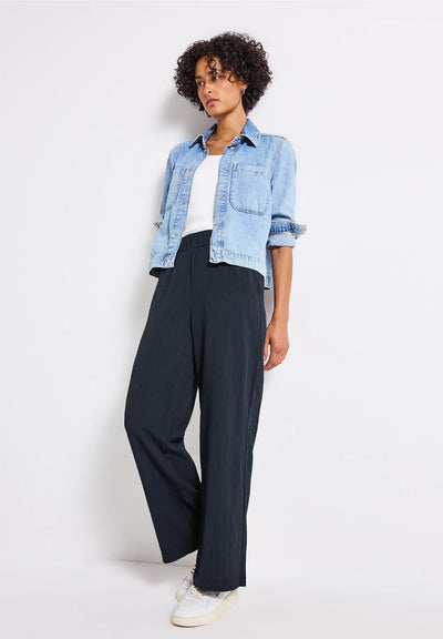 Person wearing a light blue denim jacket, white shirt, and dark pants on a white background