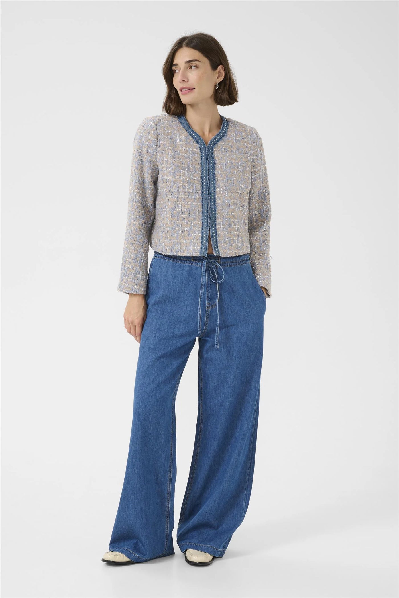 Woman wearing a gray cardigan and blue pants on a white background