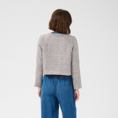 Person wearing a patterned light gray jacket and blue jeans on a white background