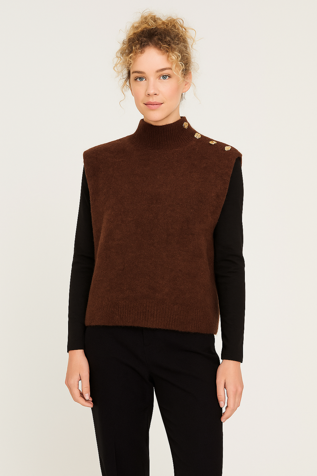 Woman wearing a brown vest over a black long-sleeve shirt on a white background
