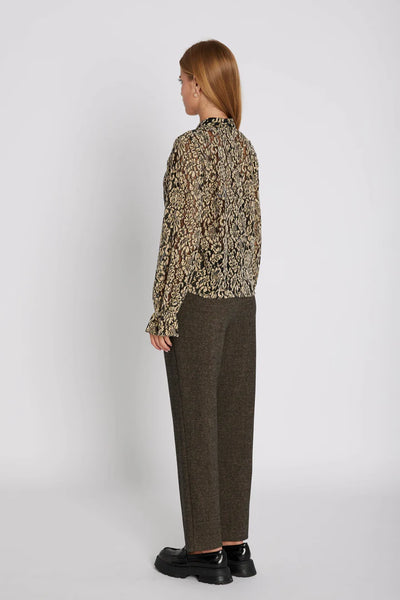 Person wearing a patterned blouse and brown pants on a white background