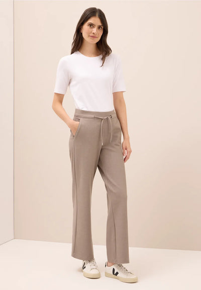 Woman wearing a white top and beige pants against a plain background