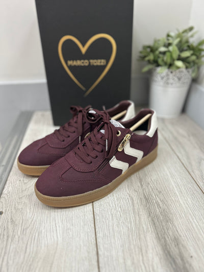 Maroon sneakers with white zigzag pattern on a wooden floor, with a black box featuring a gold heart logo in the background.
