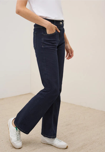 Person wearing dark blue jeans and white sneakers on a neutral background