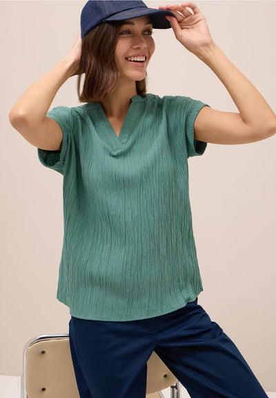 Woman wearing a green ribbed sweater and blue cap against a beige background