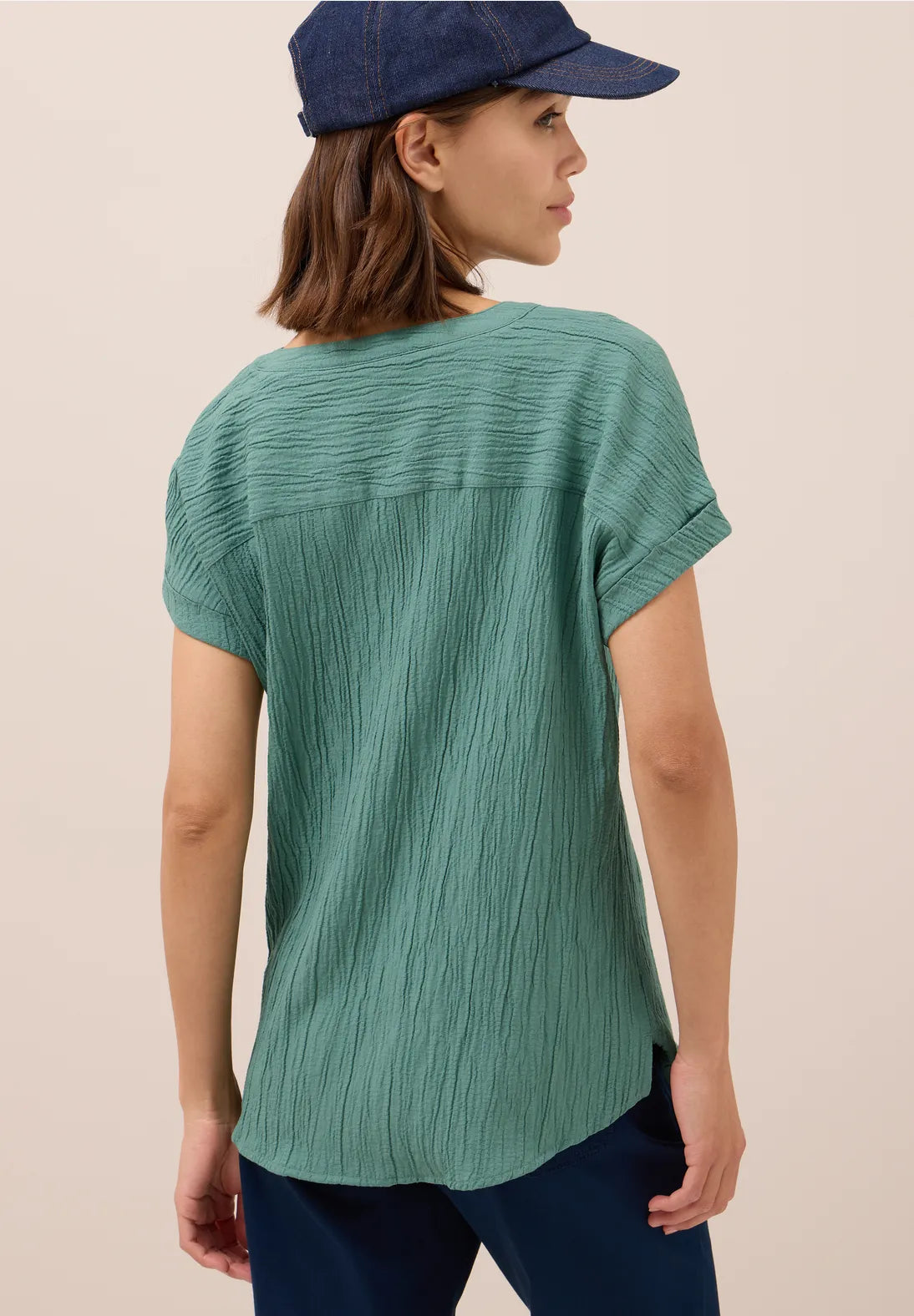 Woman wearing a green textured top and navy cap on a beige background