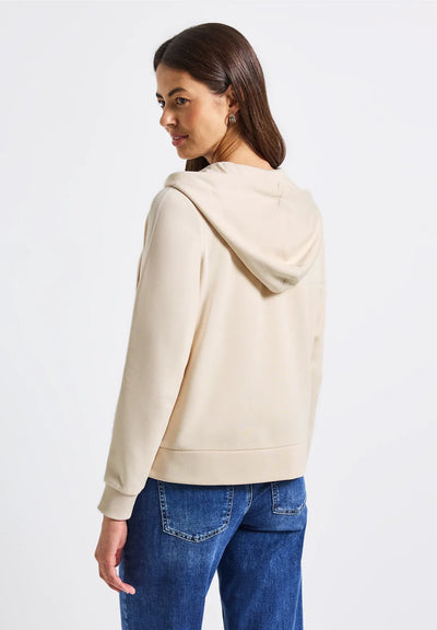 Woman wearing a beige hoodie and blue jeans on a white background
