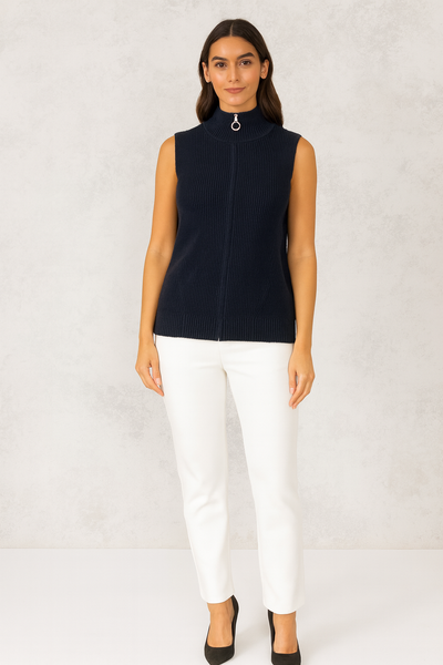 Woman wearing a navy sleeveless sweater and white pants on a light gray background