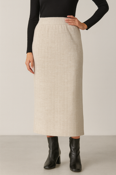 Person wearing a beige ribbed skirt with black boots on a plain background