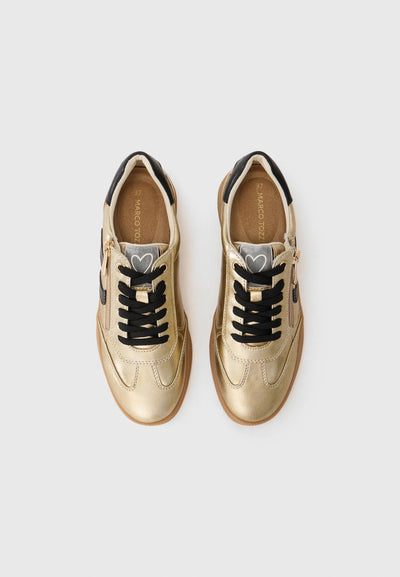 Pair of gold sneakers with black laces on a light gray background