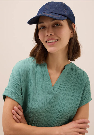 Woman wearing a teal shirt and blue cap against a beige background