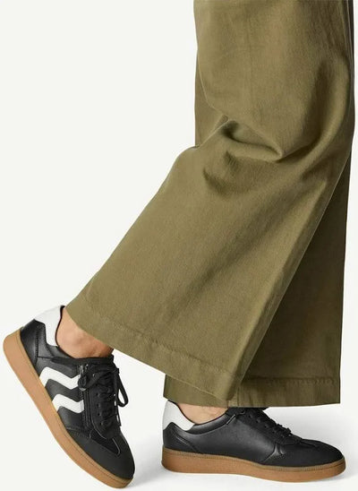 Person wearing black sneakers with white soles and brown soles, paired with green pants on a white background.