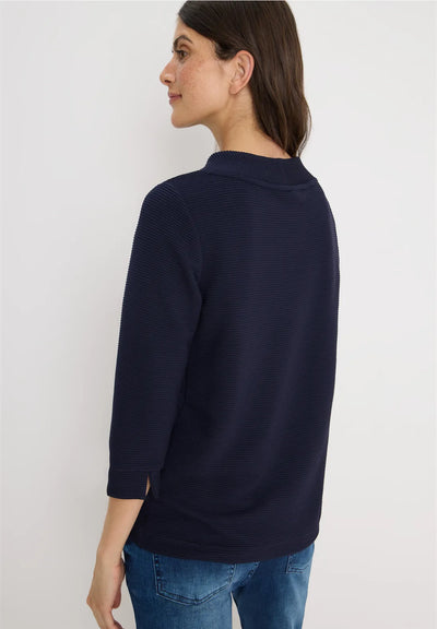 Woman wearing a navy sweater and blue jeans against a white background