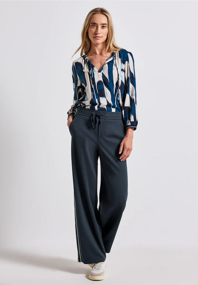 Woman wearing a patterned blouse and dark pants on a white background